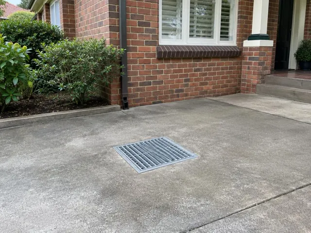 Concrete driveway with a clean metal drain grate beside a brick house in Hornsby