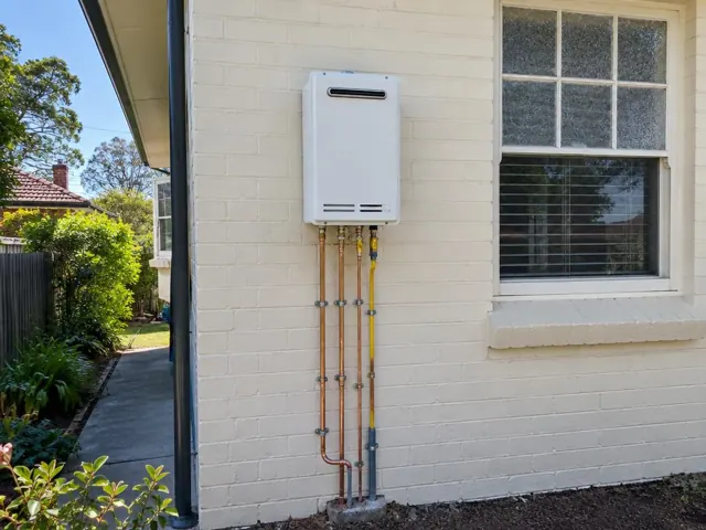 Wall-mounted hot water unit with copper pipework on an exterior brick wall beside a window in Normanhurst
